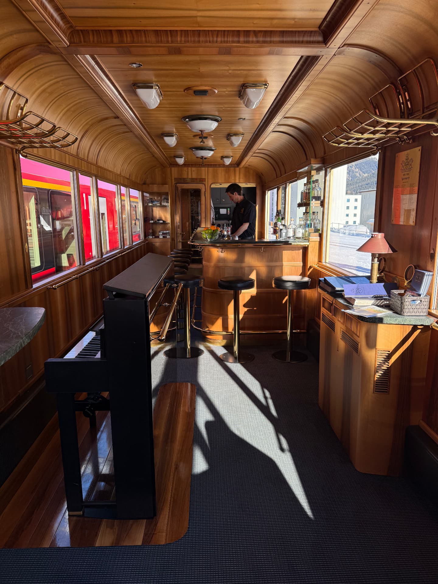 Piano Bar wagon in warm daylight, with upright piano, curved bar and brass luggage racks